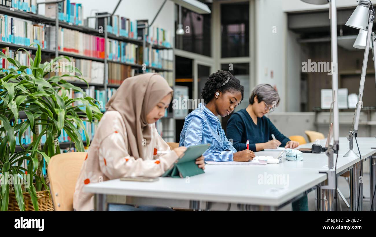 Multiethnic group of students sitting in a library and studying ...