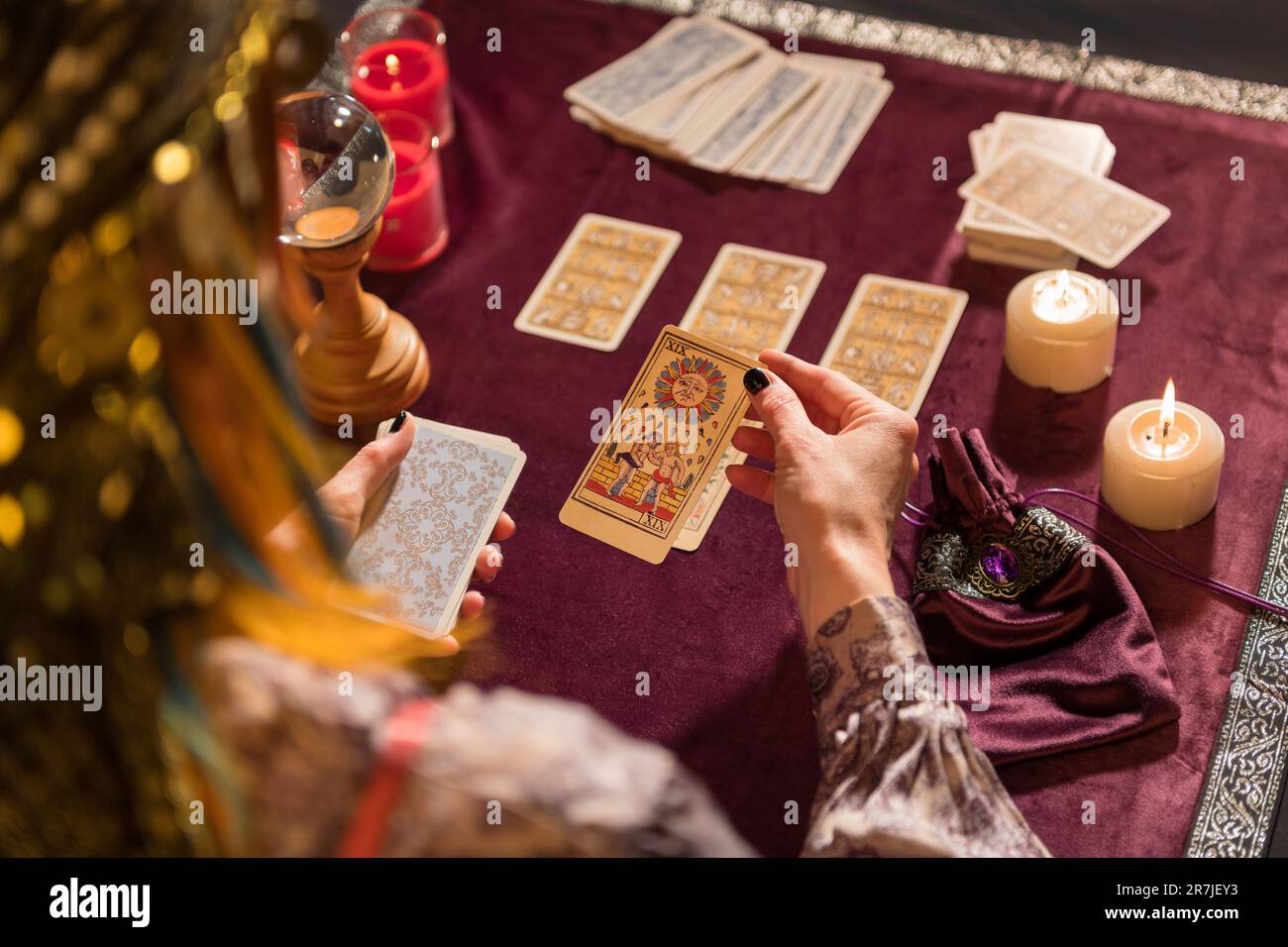 High angle of crop anonymous female fortune teller picking sun tarot card while sitting at table with burning candles and crystal Stock Photo