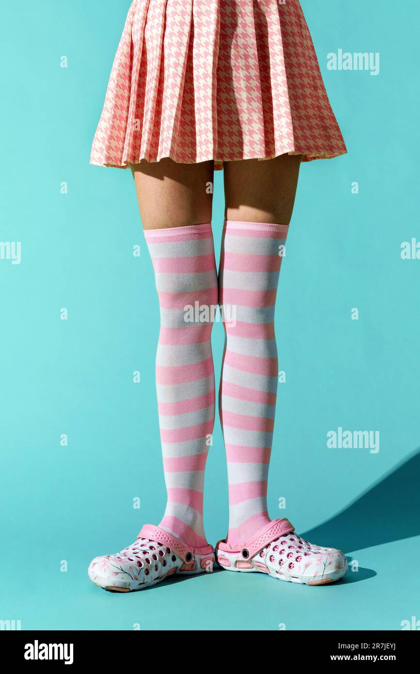 Anonymous young woman wearing checkered dress and long pink striped socks with shoes while standing on turquoise floor with shadow Stock Photo