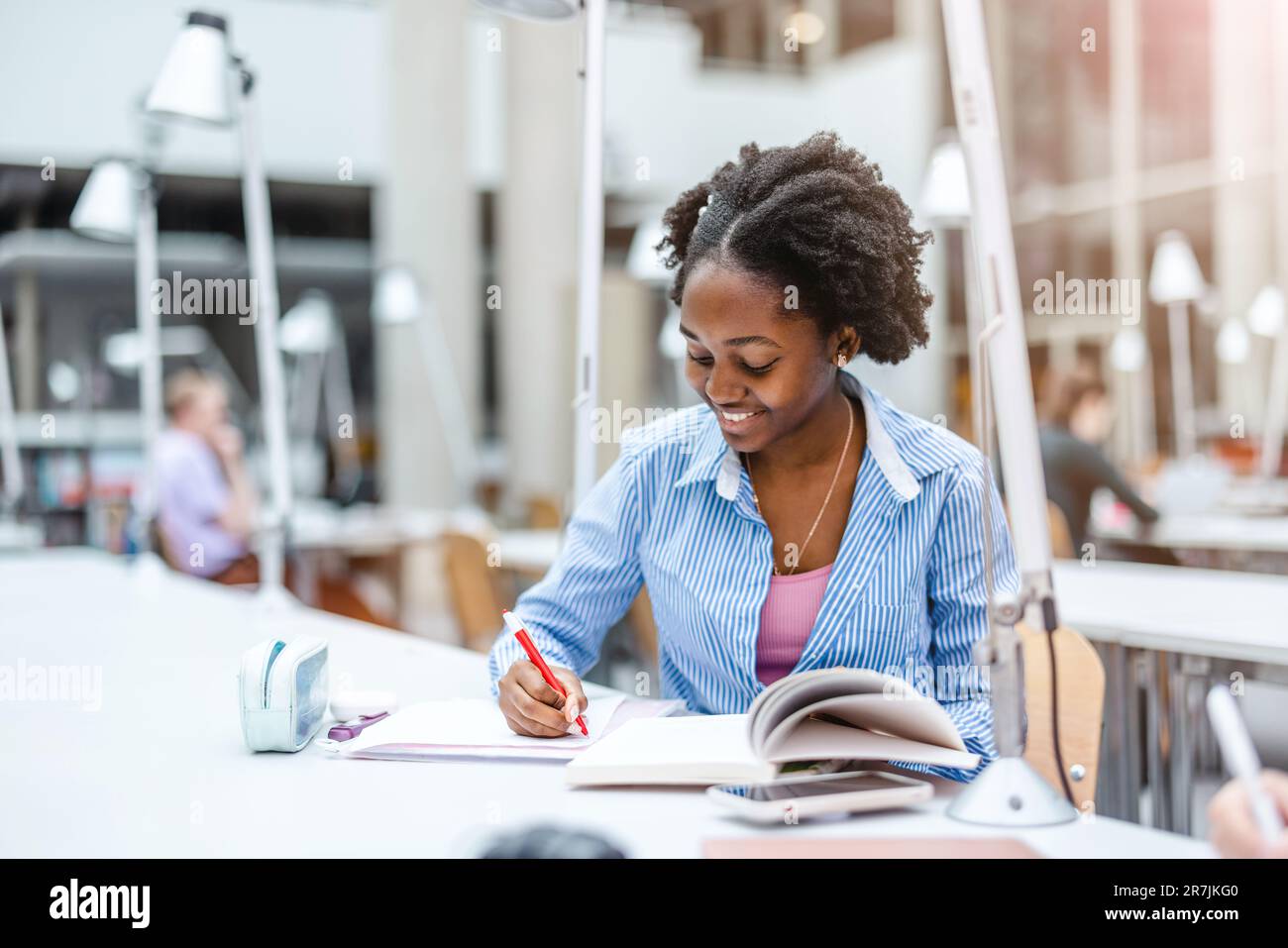 Young black woman writing in notebook in a library Stock Photo - Alamy