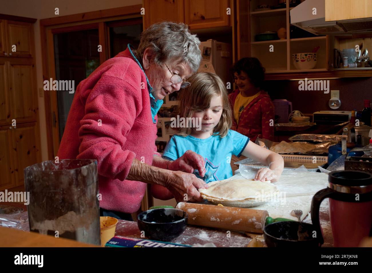 A nine-year old girls helps her grandmother put the finishing touches on a homemade berry pie in a cottage in Ontario, Canada. Stock Photo