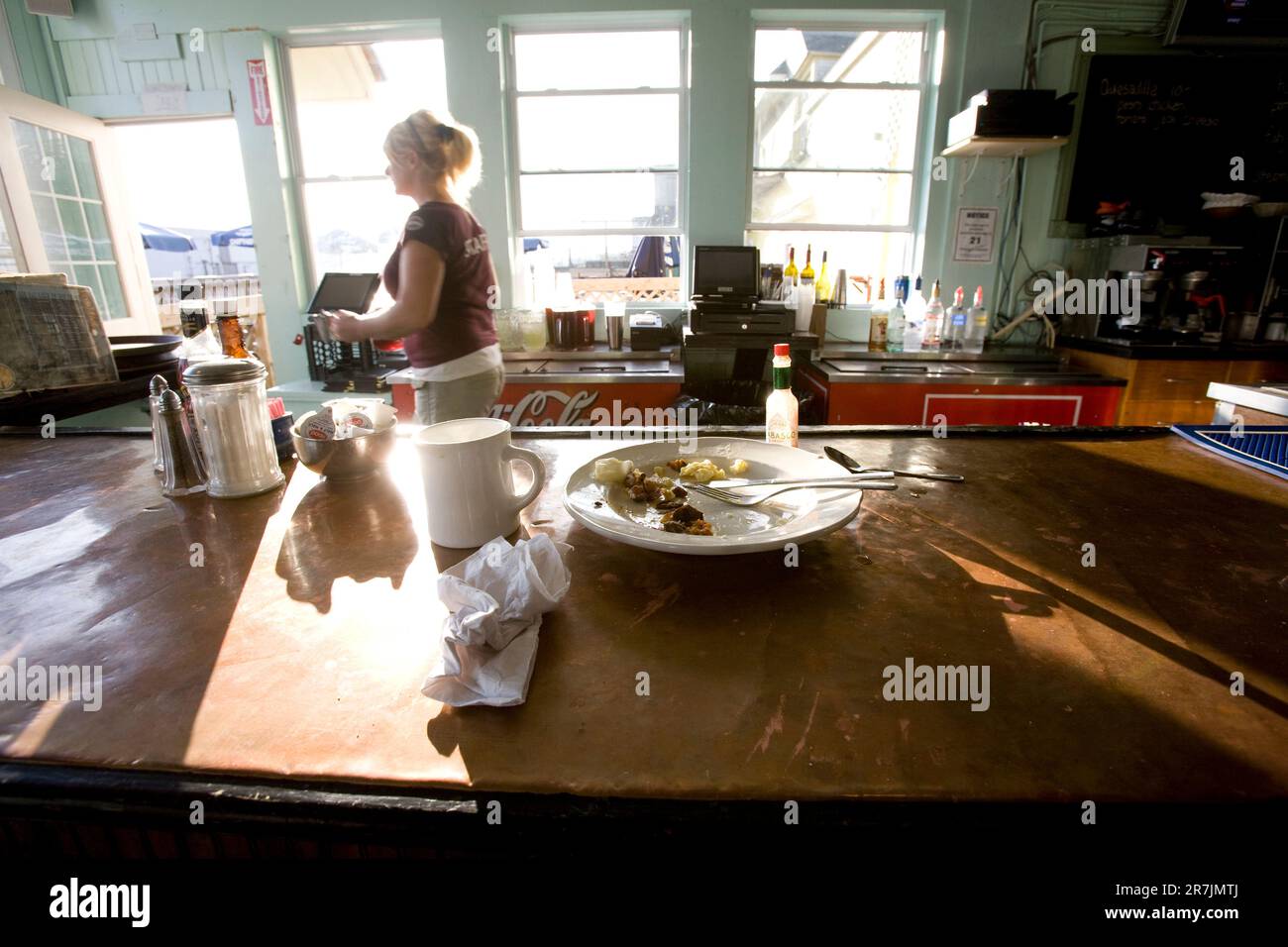 Half eaten plate of food sits at the empty bar of a local seafood restaurant in Portland, ME as a waitress passes in the background. Stock Photo