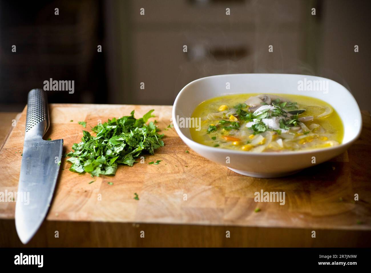 A homemade bowl of hot Thai Tom Kha soup sits next to a knife and fresh organic cilantro on a countertop in Seattle, Washington. Stock Photo