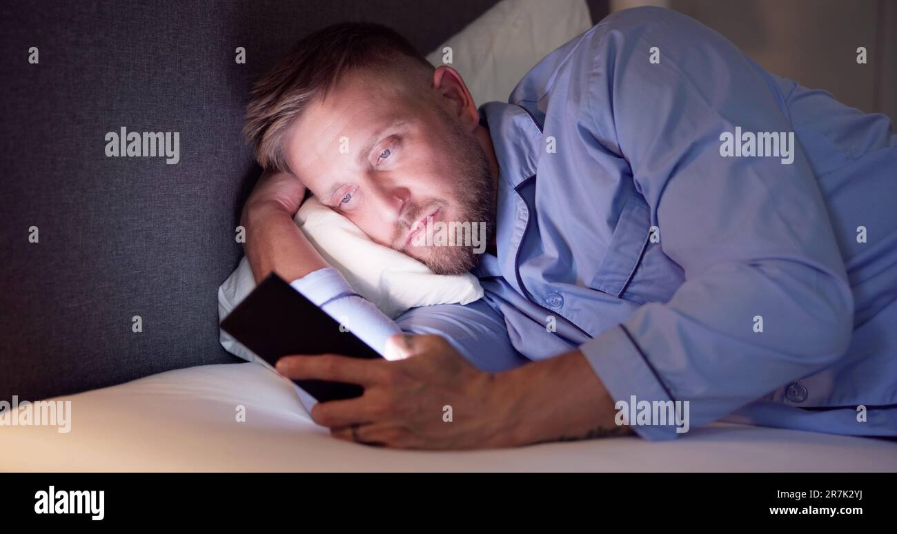 Man Lying On Bed Using Mobile Phone At Night Stock Photo