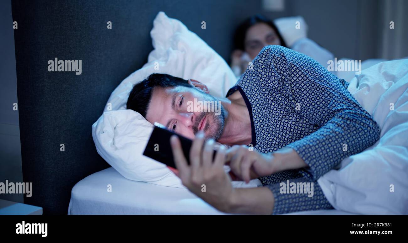 Young Man Using Cellphone While Her Wife Sitting On Bed At Night Stock Photo
