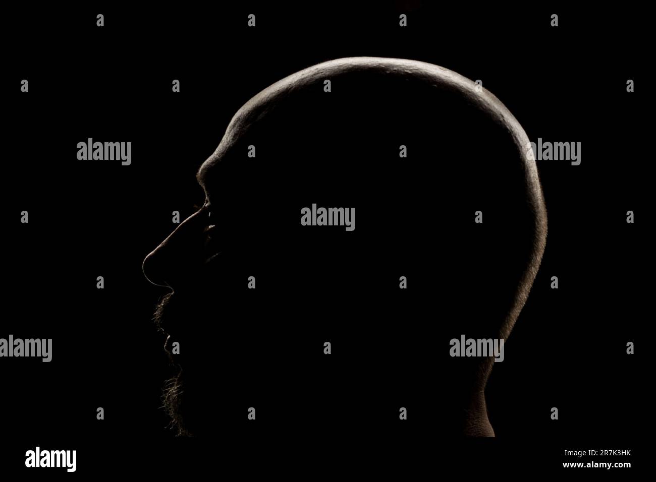 Silhouette of a man head in backlight. Low light portrait. Isolated on dark background. Stock Photo