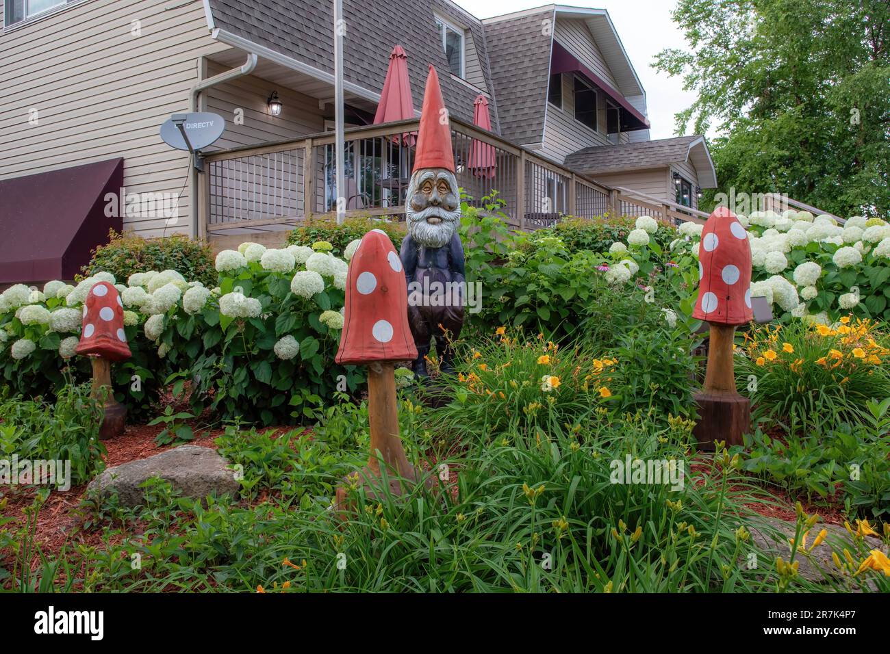 Wooden gnome and mushrooms among beautiful snowball bush viburnum and orange lilies on a summer day at Sven Factory Outlet Store in Chisago City, Minn Stock Photo