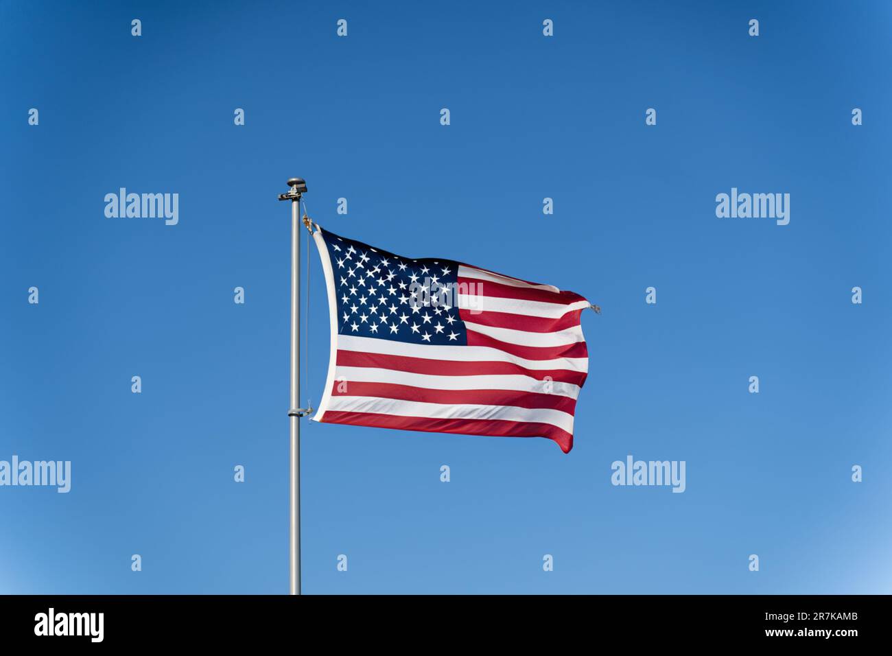 The flag of the United States of America flutters in the wind against a clear blue sky. Waving USA flag Stock Photo