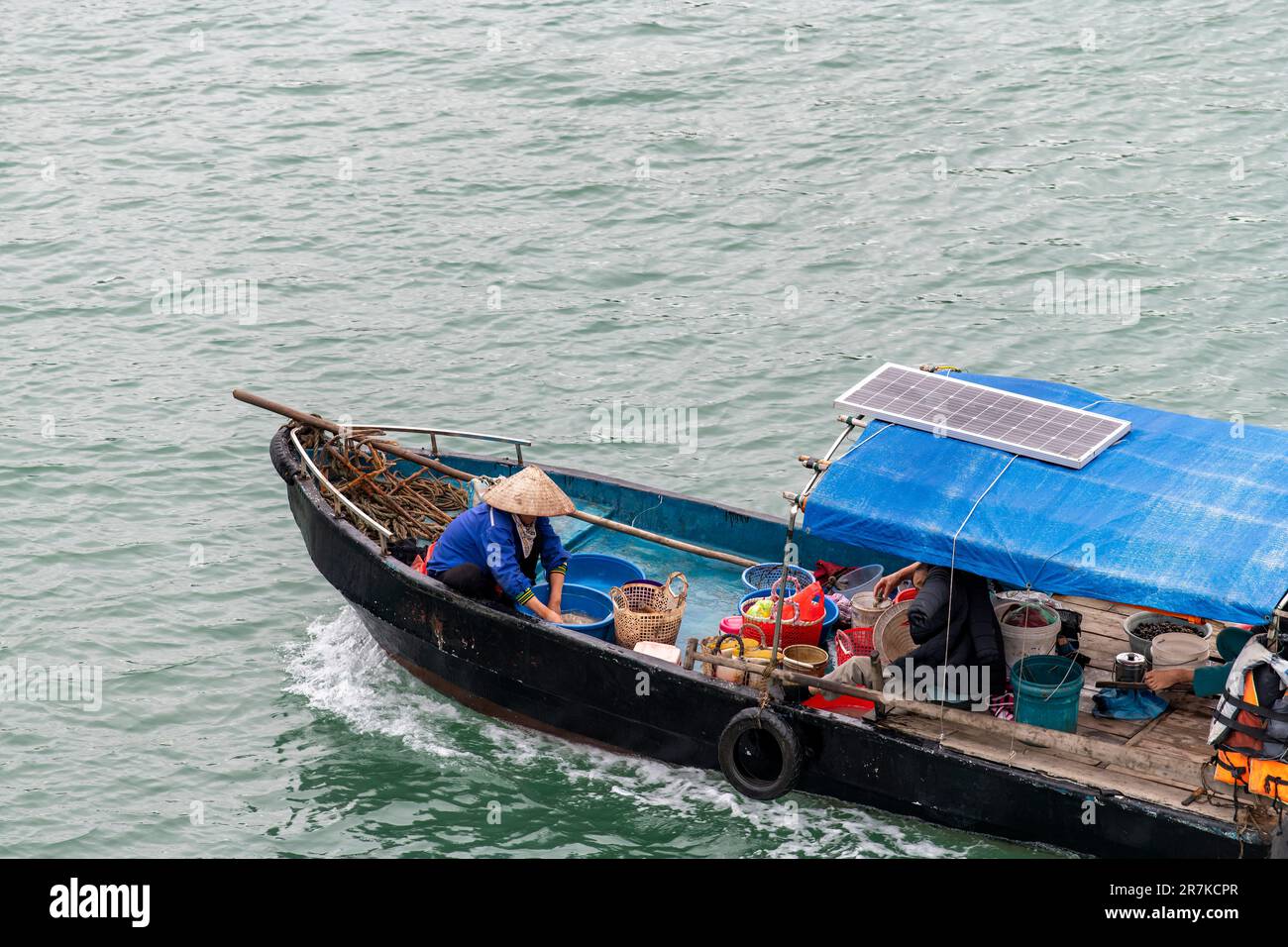 High angle close up view of a small wooden fishing boat in water of Halong Bay, Vietnam with woman with straw hat taking care of catch of the day Stock Photo
