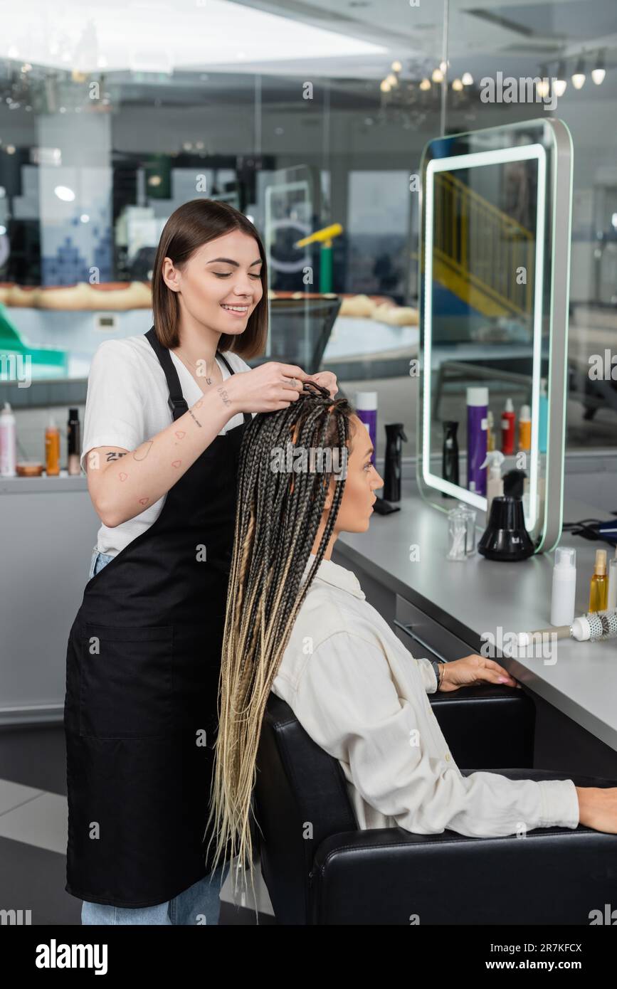 beauty industry, braids, happy hairdresser braiding hair of woman in salon, braiding process, salon customer, beauty profession, client satisfaction, Stock Photo