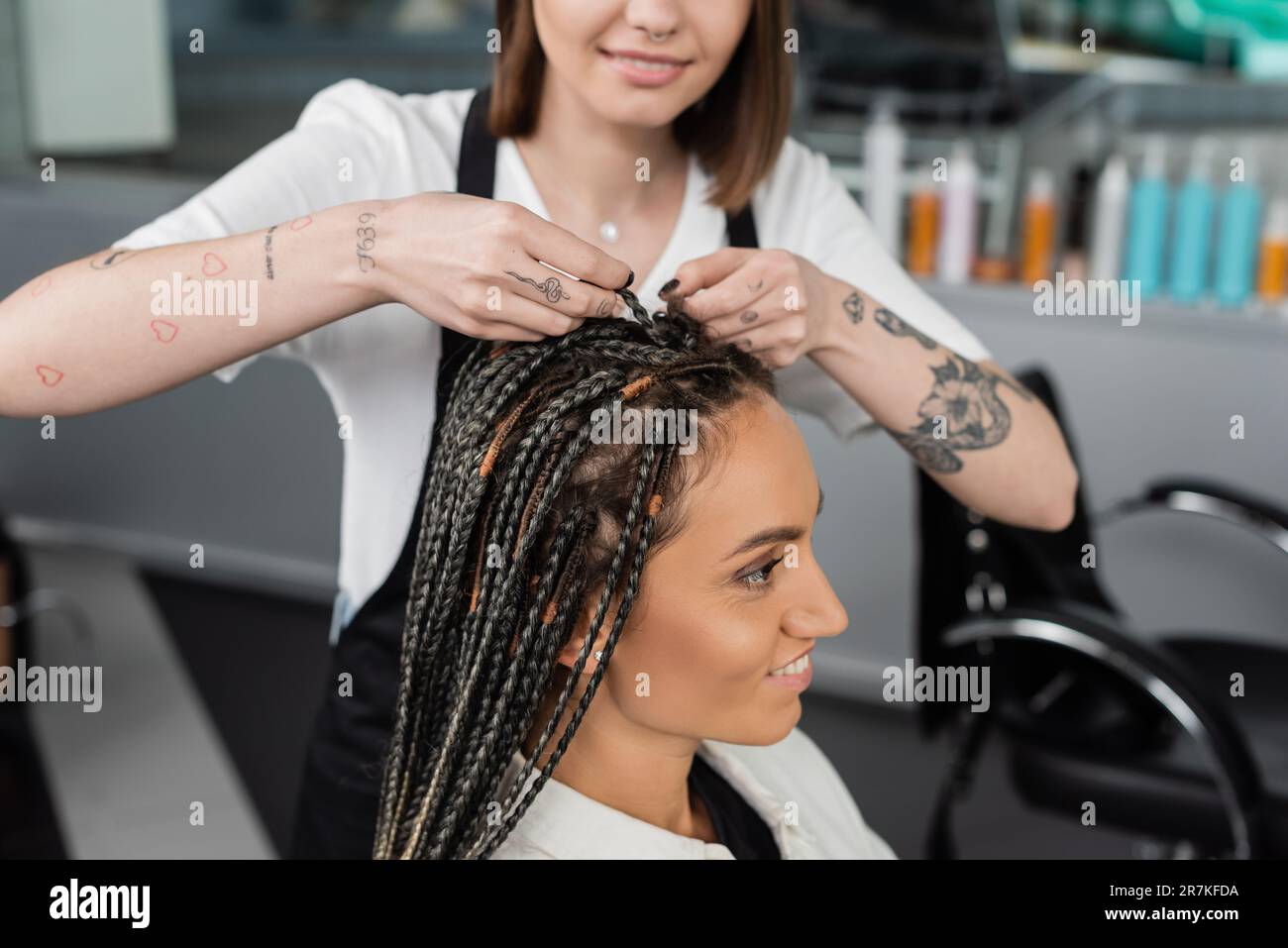 beauty industry, braids, tattooed hairdresser braiding hair of woman in salon, braiding process, salon customer, beauty profession, client satisfactio Stock Photo