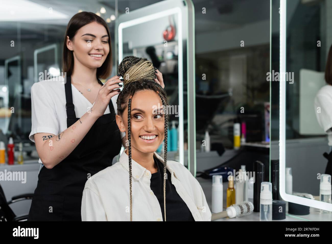 hair make over, happy hair stylist doing hair bun to female client with braids, cheerful women, client satisfaction, customer in salon, beauty service Stock Photo