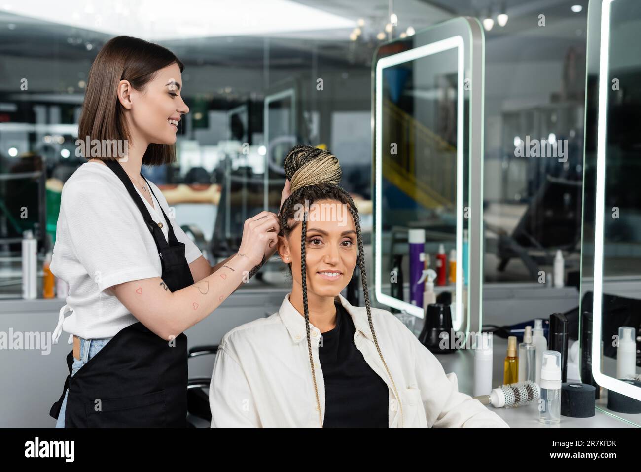 salon experience, happy hair stylist doing hair bun to female client with braids, cheerful women, client satisfaction, customer in salon, beauty servi Stock Photo