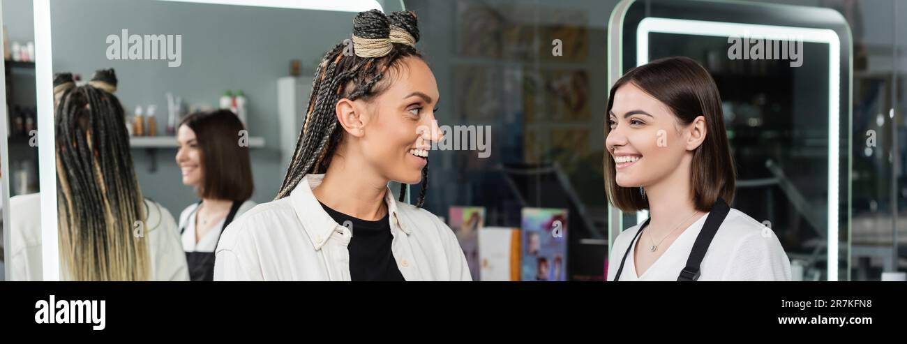 client satisfaction, hairdresser smiling with female customer, happy woman with braids, hairstyle, hair buns, braided hair, beauty salon, professional Stock Photo