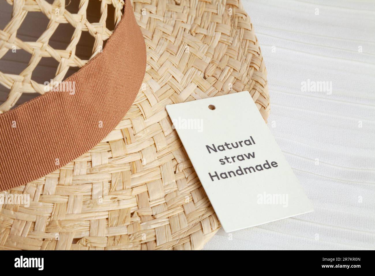 Real natural straw hat with a brown ribbon and a tag in a fashion store. New yellow woven sunhat for sale in a headwear shop window - Stock Image