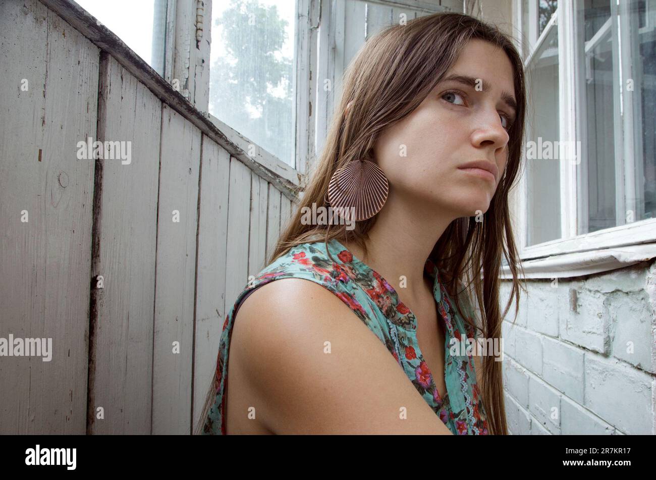 Natural beauty of a young woman dressed in a vintage outfit in a grungy interior. Sad melancholic Caucasian lady wearing boho chic clothing in a rusti - Stock Image