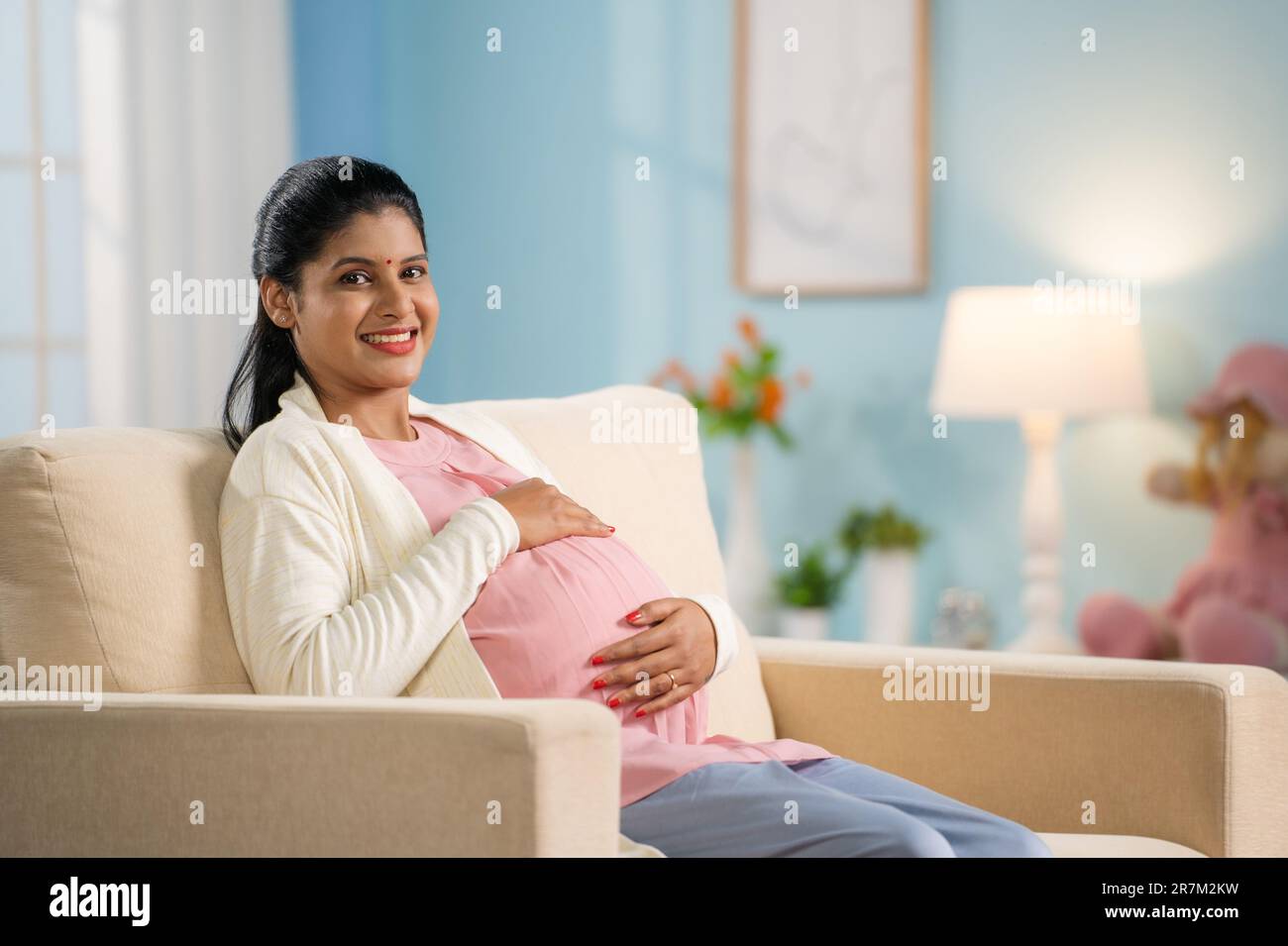 Happy smiling pregnant woman looking camera by touching or feeling tummy - concept of Expecting mother, Prenatal connection and motherhood Stock Photo