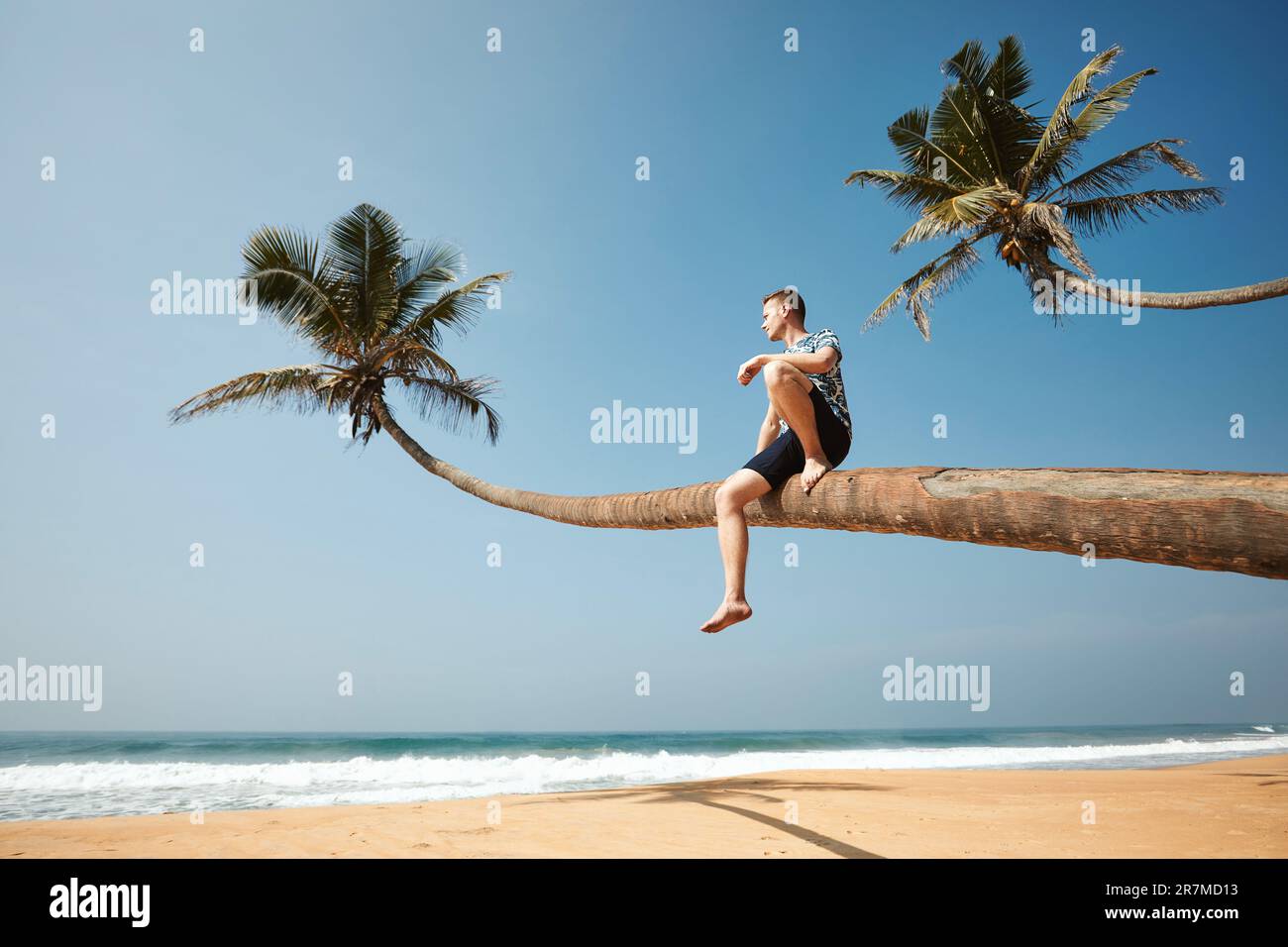 Man sitting on trunk of palm tree and enjoying sea view. Idyliic sand beach in Sri Lanka. Stock Photo