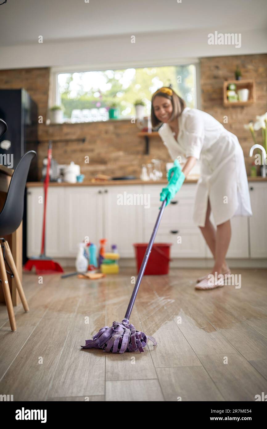 Joyful housewife cleaning the kitchen, wet mopping the floor, with