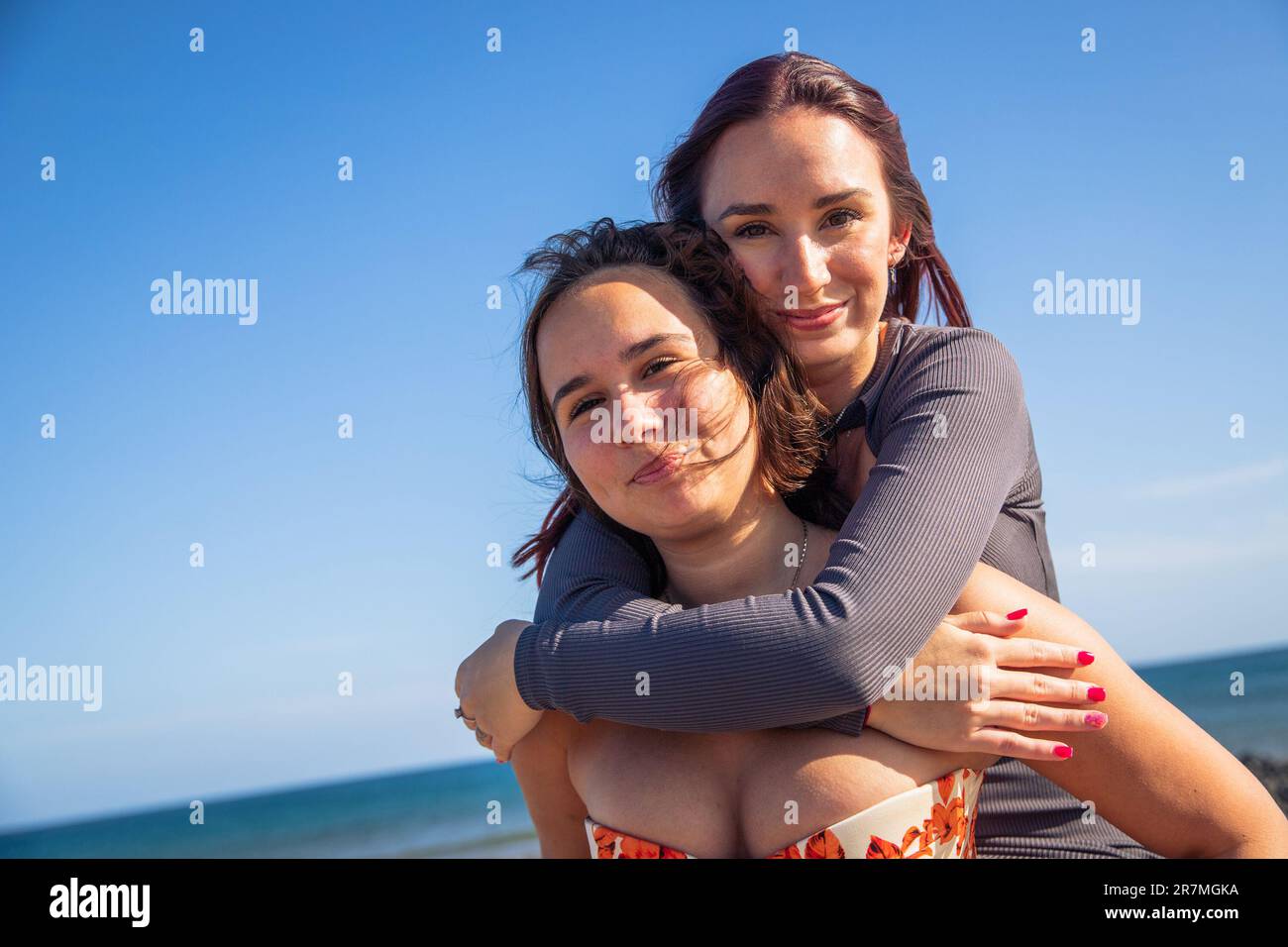 Two sisters have fun together, one lifts the other on her back at the beach Stock Photo