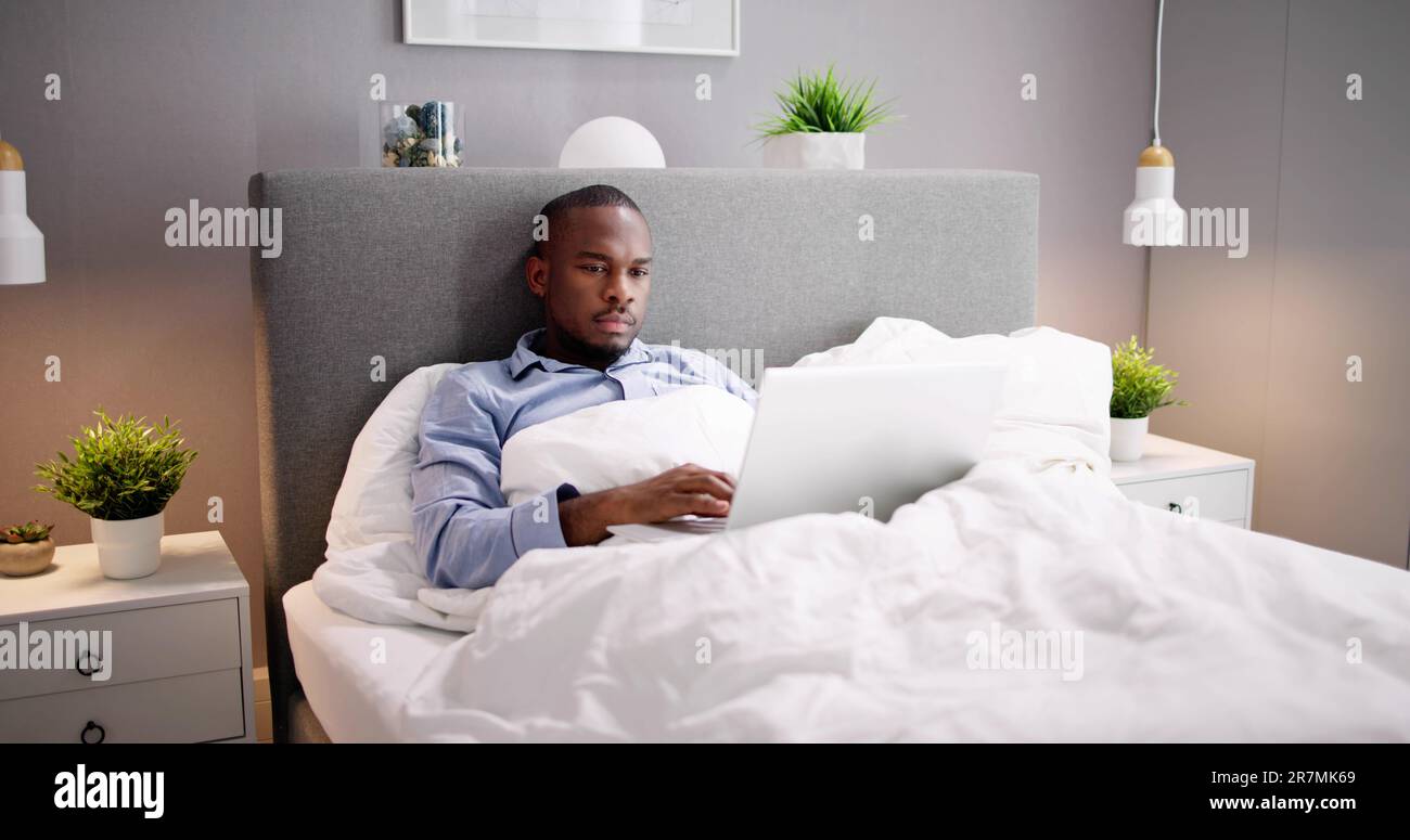 Happy Man Sitting On Bed Using Laptop Stock Photo
