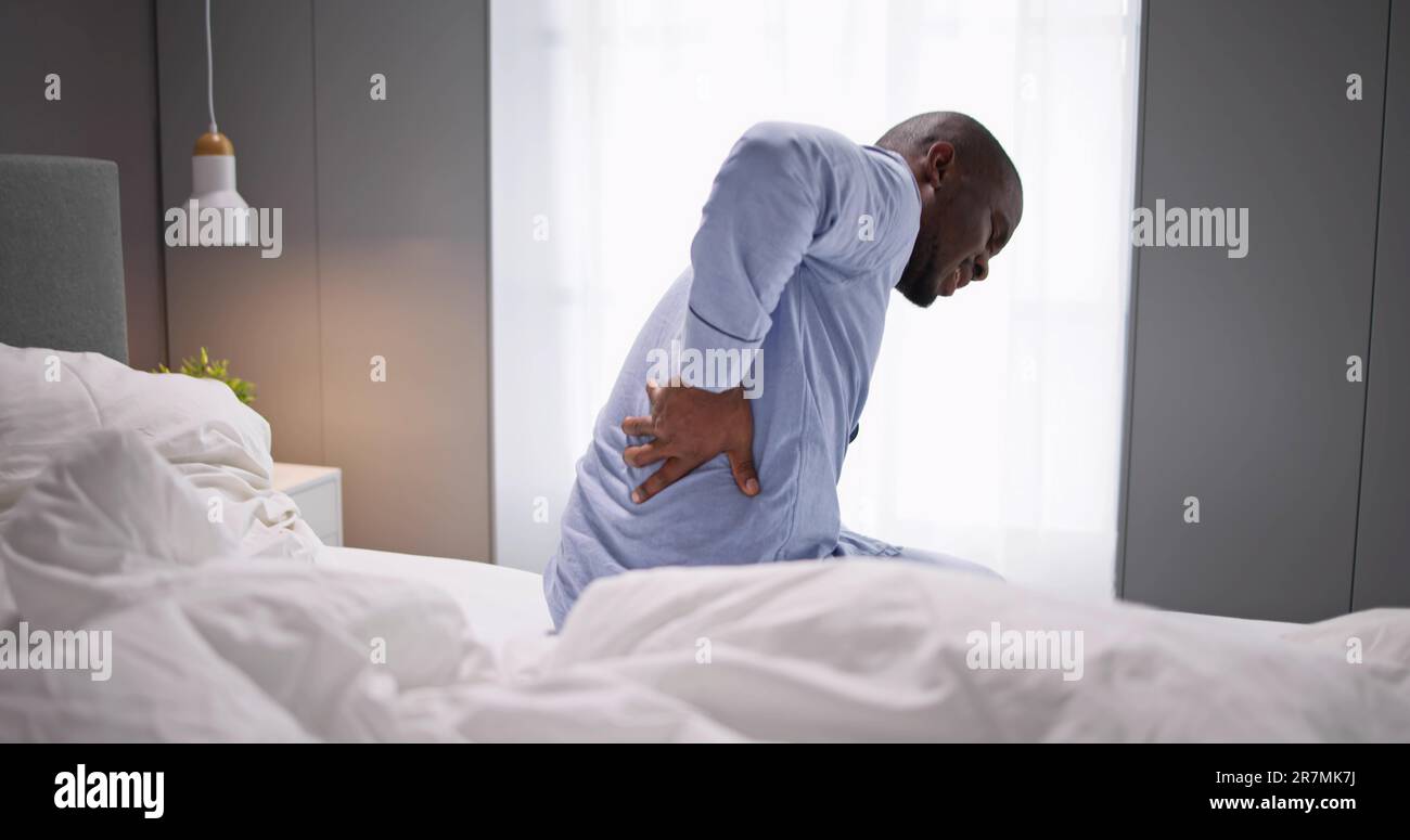 Man Sitting On Bed Suffering From Back Pain Stock Photo - Alamy