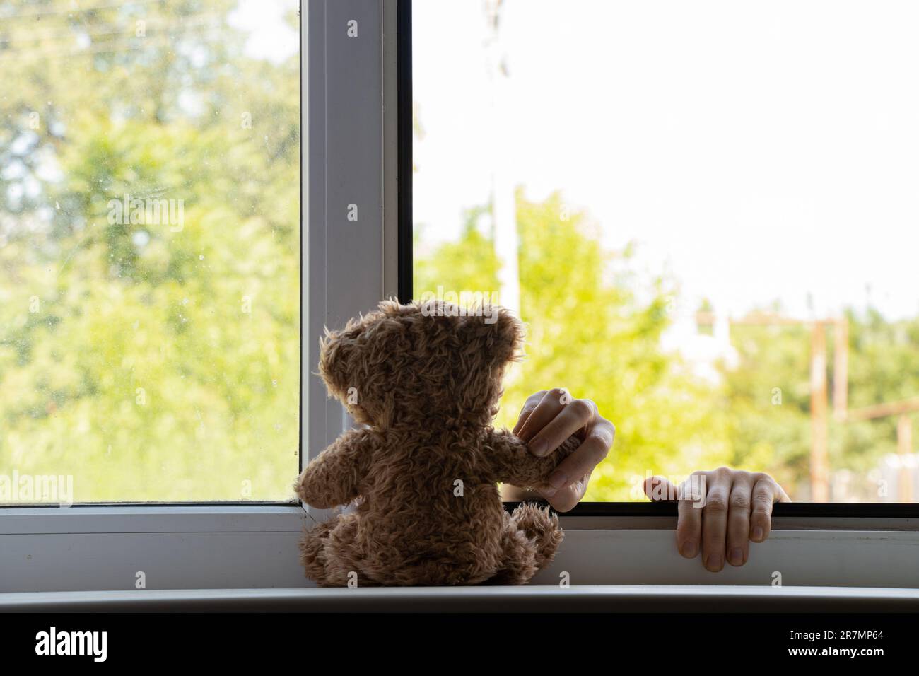Children's hands hold on to the window from the side of the street and hold a teddy bear, suicide, hands outside the window, suicide Stock Photo