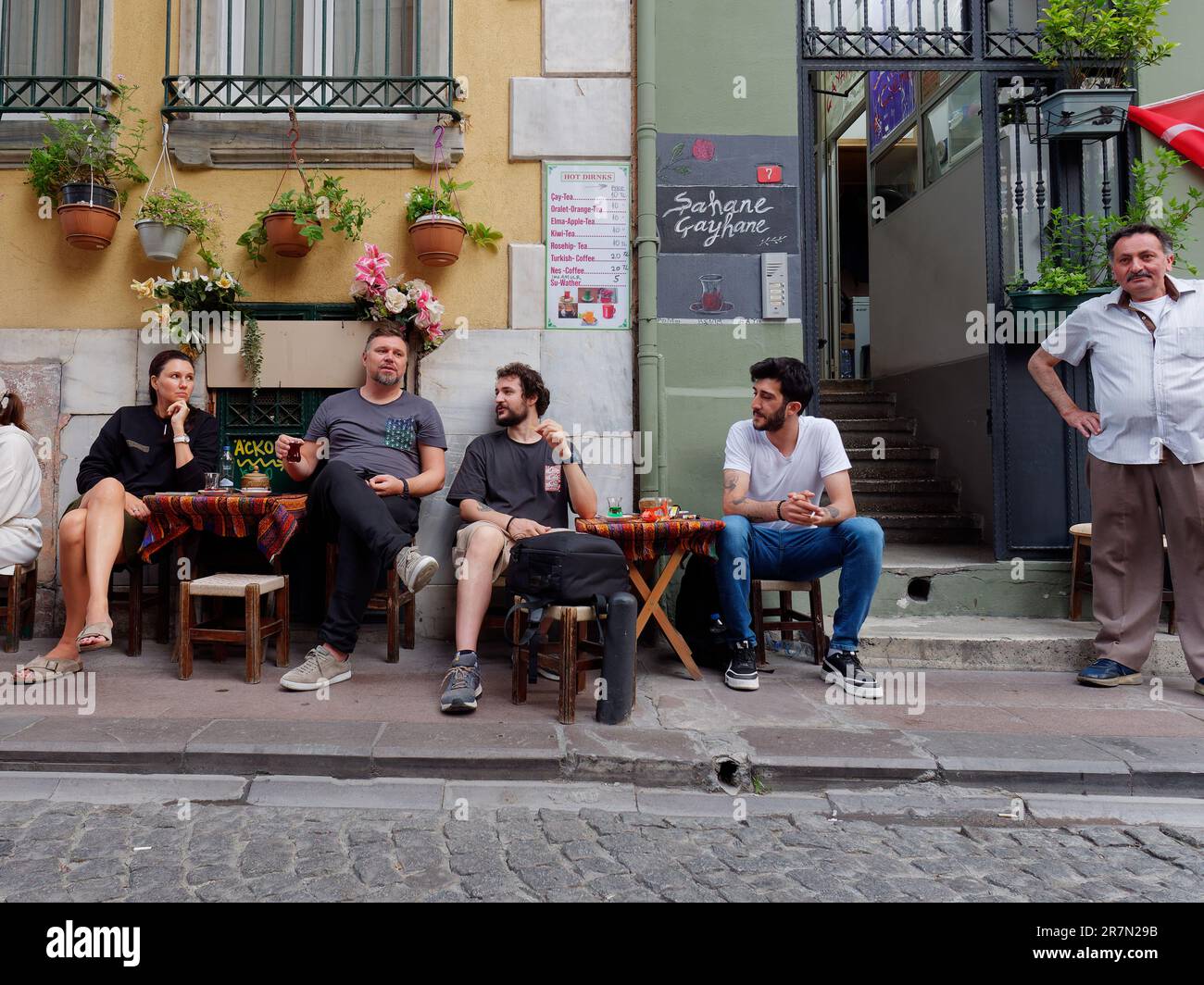 Friends enjoying a Turkish tea on informal table and chairs on a pavement in a quaint street with flower pots in the Galata area of Istanbul, Turkey Stock Photo