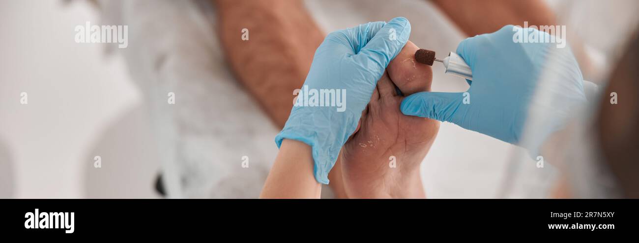 Pedicure master removes dry skin from toe of man with grinding tool in salon Stock Photo