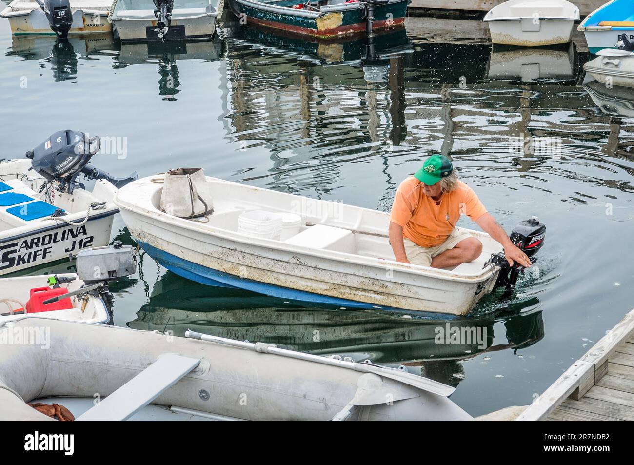 Man with his new outboard motor,is not sure about how it works. So he made big turn, only to hit a boat tied to the wharf.  Bad start to the day. Stock Photo