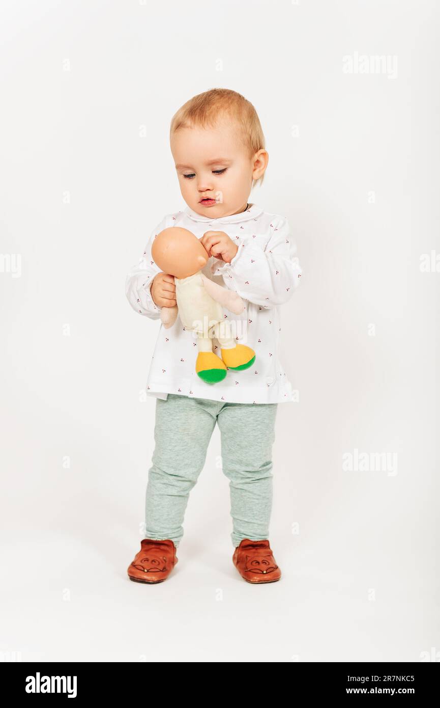 Studio shot of adorable 1 year old baby girl taken on white background, holding a doll Stock Photo