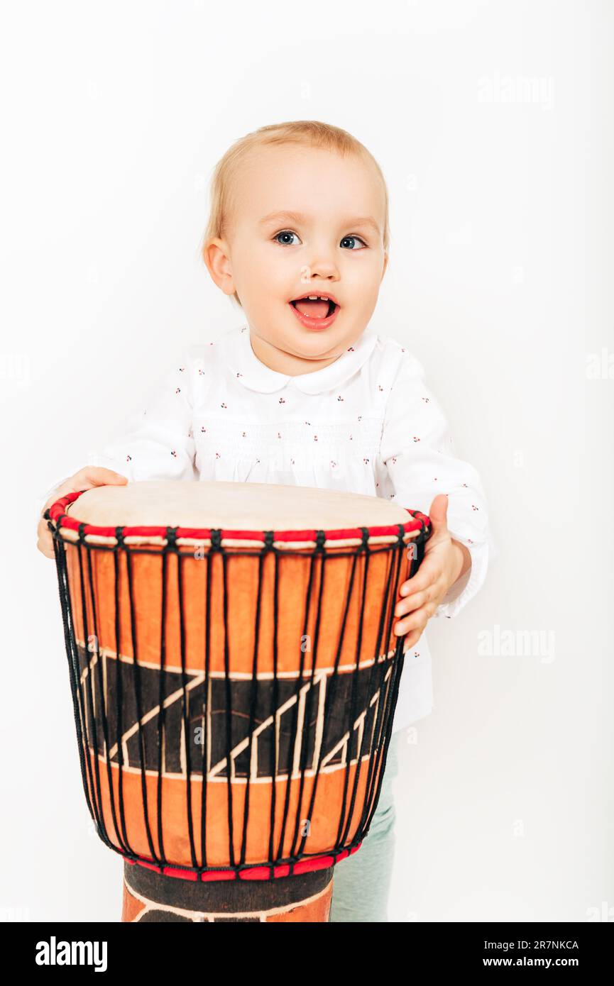 Cute toddler baby girl playing ethnic drum, studio shot on white background Stock Photo