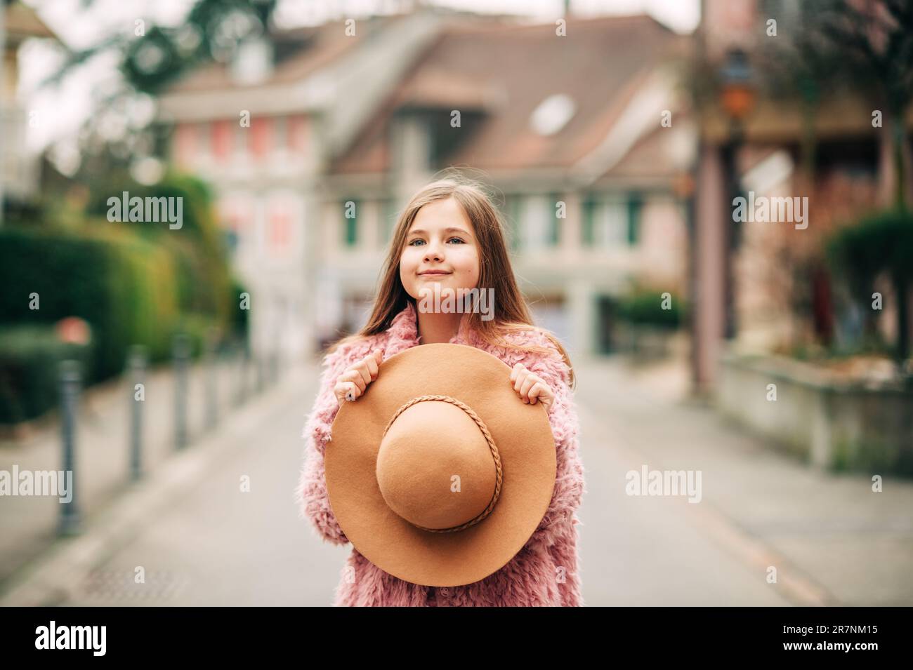 Outdoor portrait of adorable young kid girl holding brown hat, spring fashion for children Stock Photo