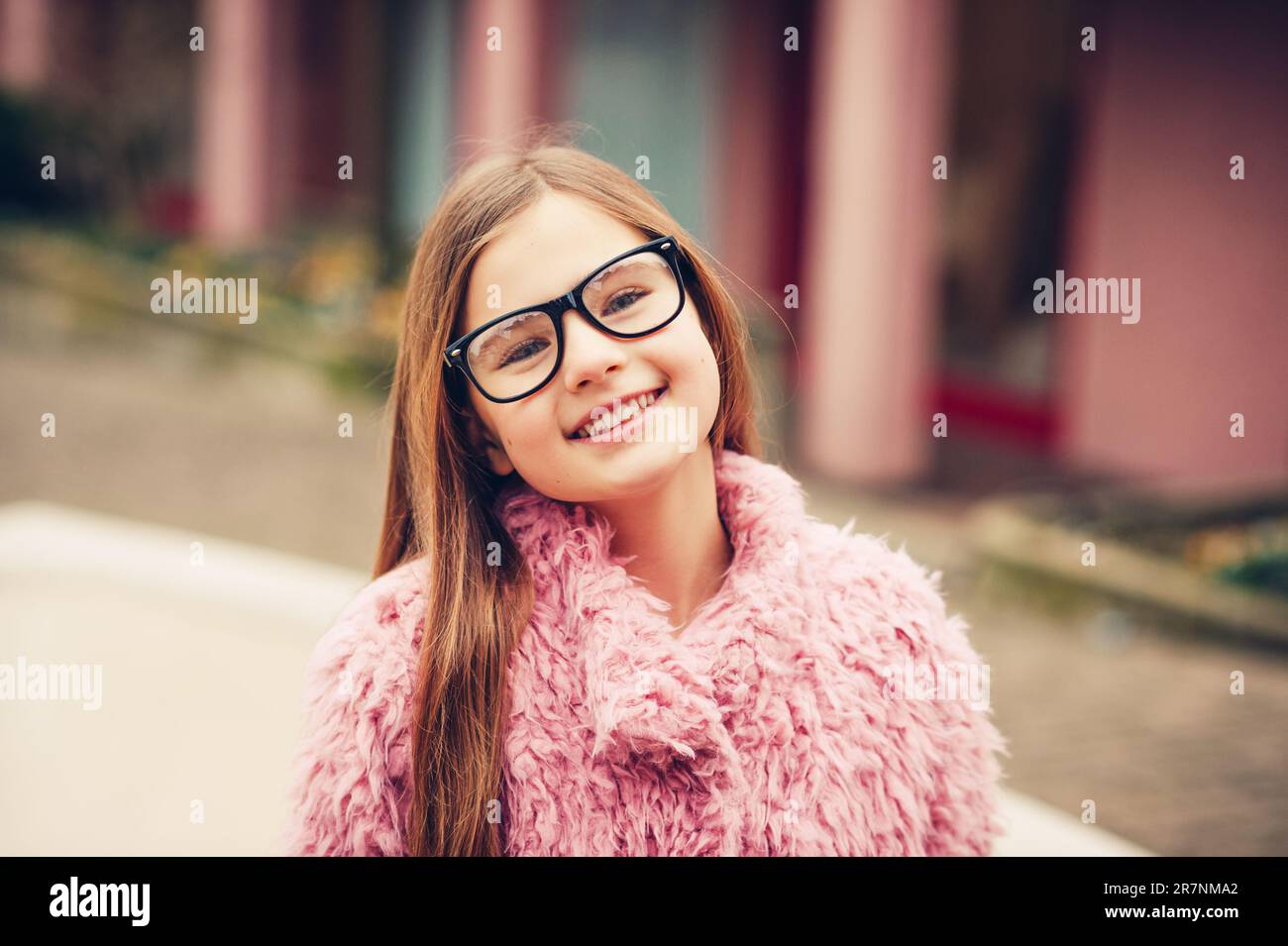 Outdoor portrait of cute young kid girl wearing eyeglasses and pink coat Stock Photo