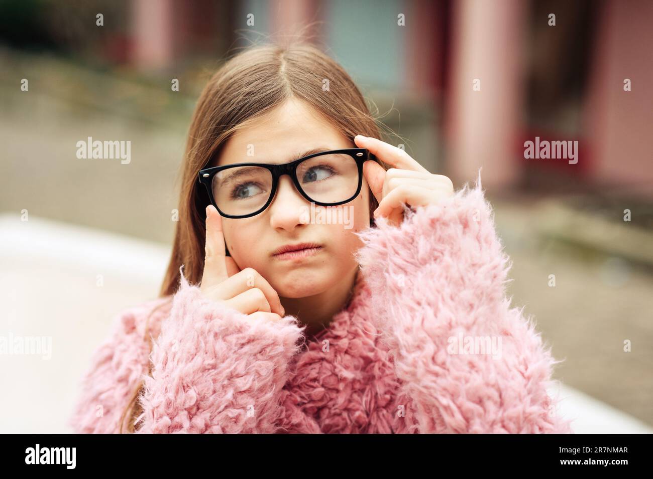 Outdoor portrait of cute young kid girl wearing eyeglasses and pink coat Stock Photo