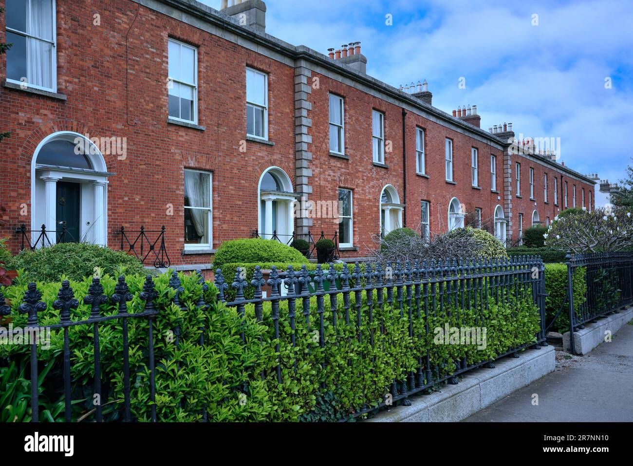 Long row of brick townhouses with iron railing fence along sidewalk Stock Photo