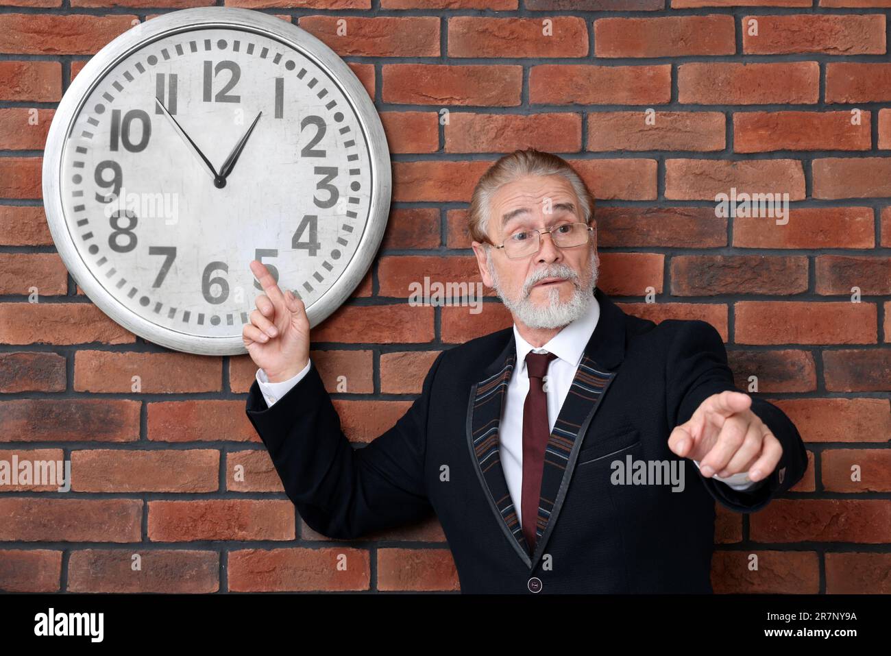 Angry senior boss pointing at clock on brick wall Stock Photo