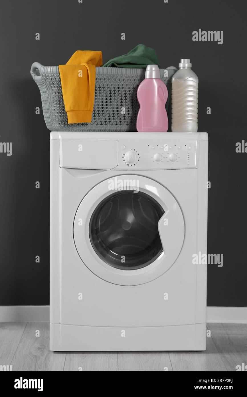 Washing machine with clothes and detergents near black wall indoors ...