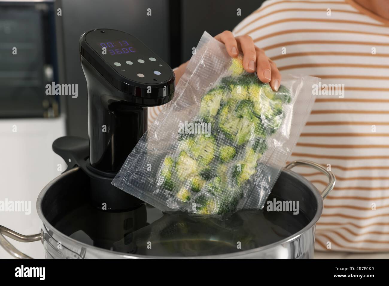 Woman putting vacuum packed broccoli into pot with sous vide cooker