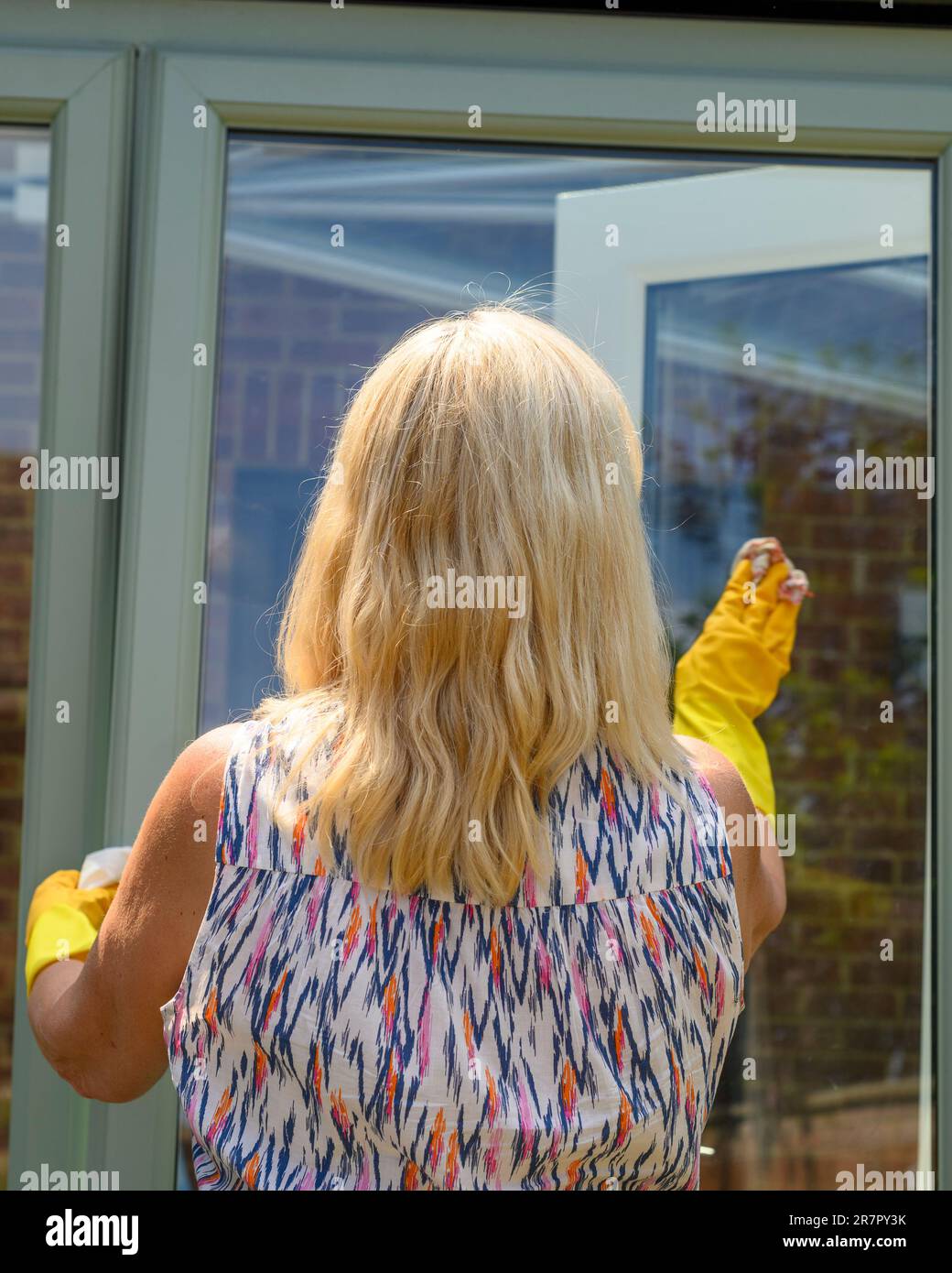 Woman wearing yellow rubber gloves cleaning windows outside Stock Photo