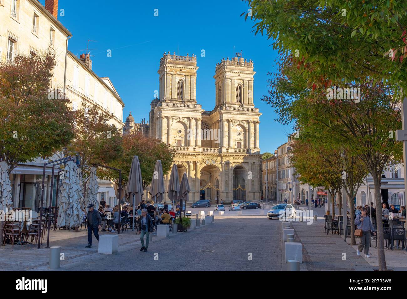 Auch, France - November 5, 2022: The Auch Cathedral steeples facing the sunset with some people sitting and walking on a busy commercial street Stock Photo