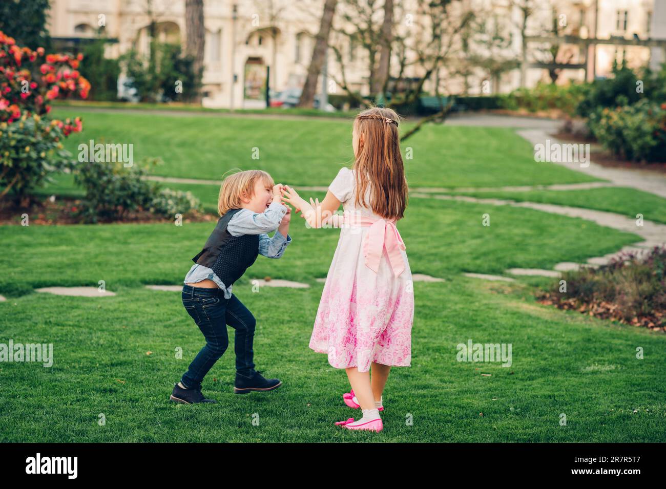 Young girl and boy playing in spring garden, wearing occasion clothes, fashion for young children Stock Photo