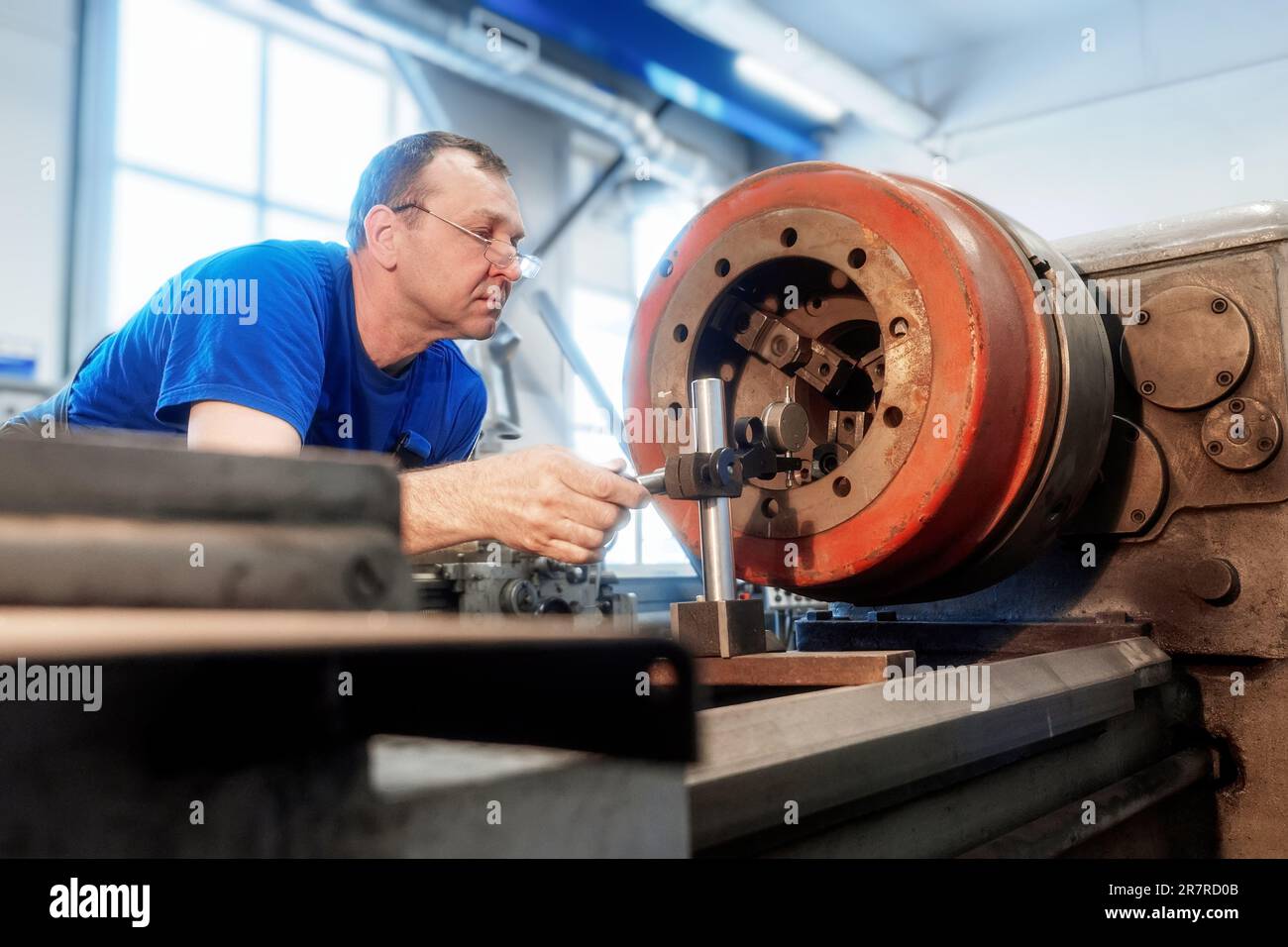 An elderly Caucasian metal turner works in a workshop behind a lathe ...
