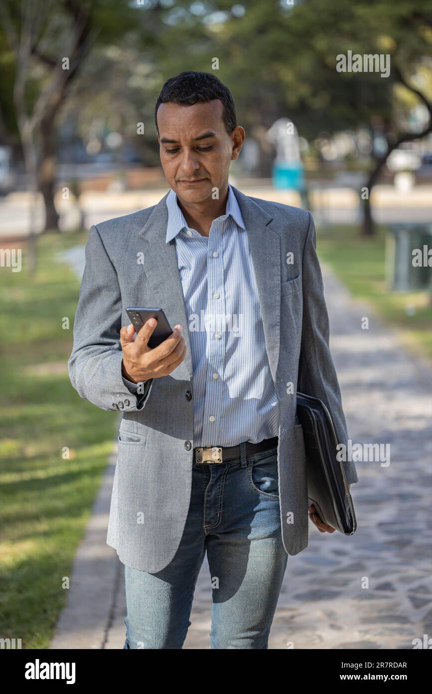 Young latin man in suit walking with mobile phone in hand. Stock Photo