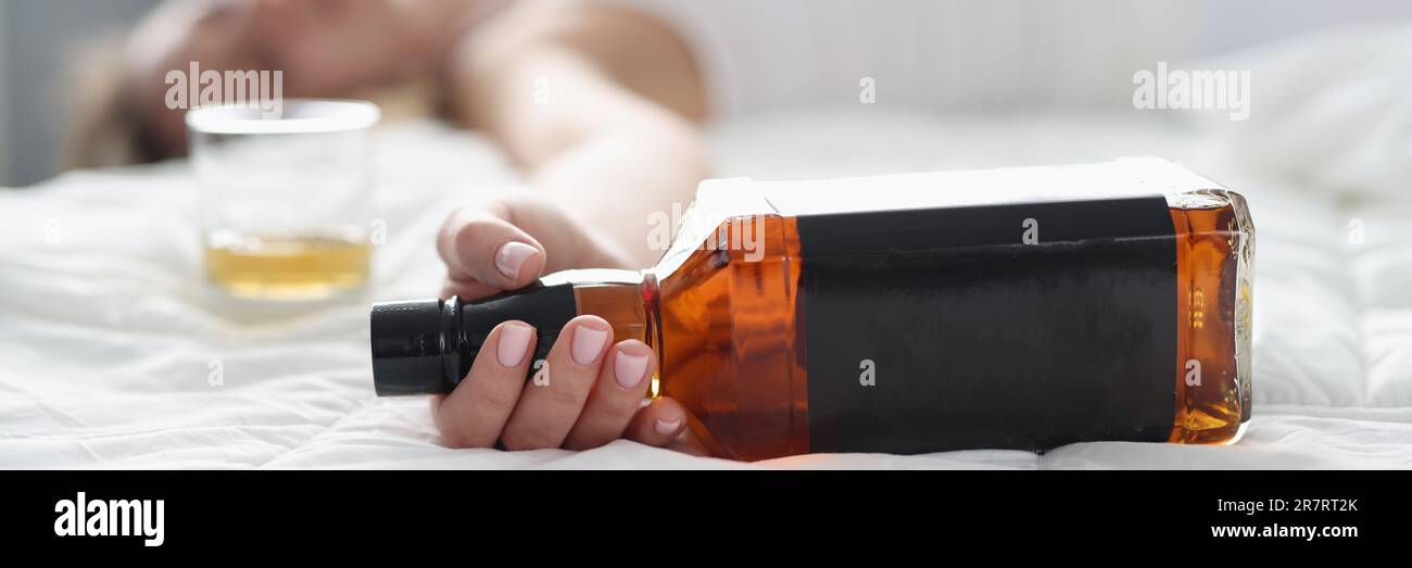 Woman lies in white bed with bottle of whiskey in hand Stock Photo