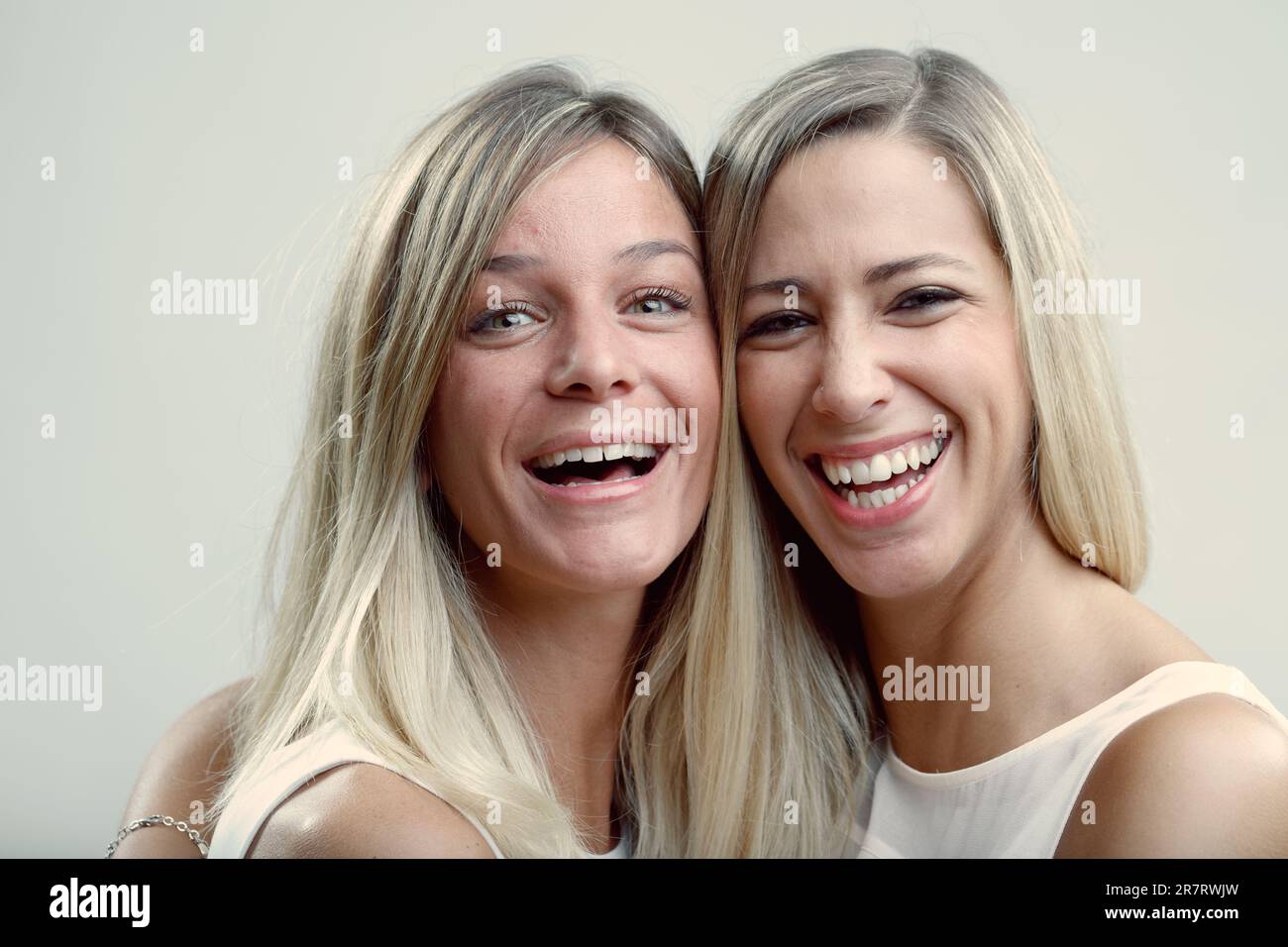 Two friendly blondes share affectionate cuddles and kisses. Their bond, akin to sisterhood, is portrayed in their pose Stock Photo