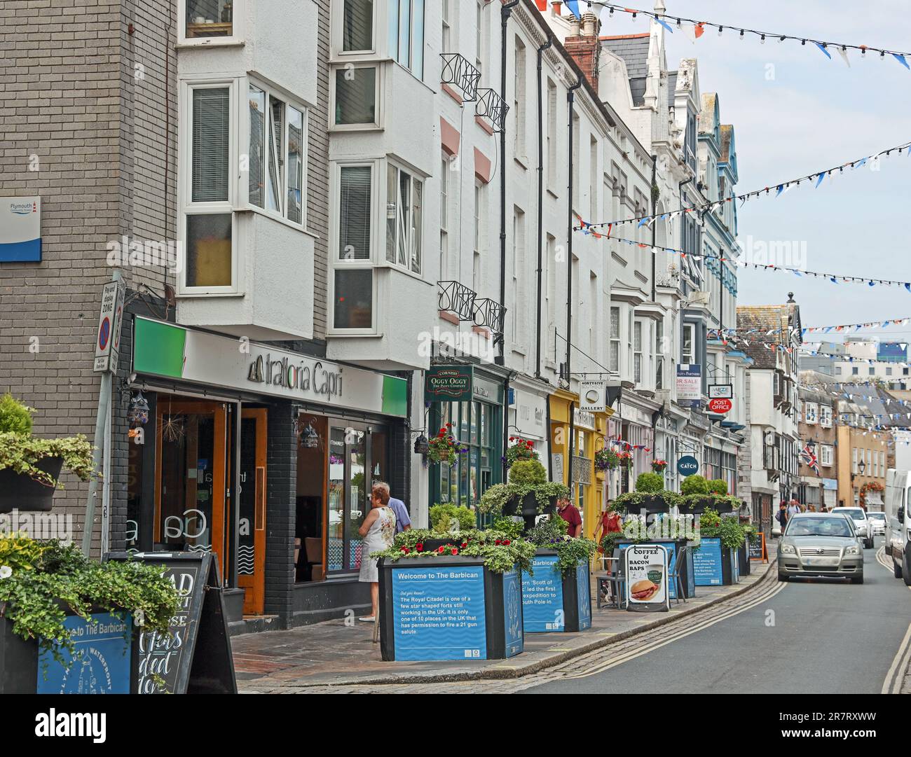 Flower tubs and bunting bring a celebratory feel to Southside Street on Plymouth’s historic Barbican. A quirky mix of small shops, public houses and r Stock Photo