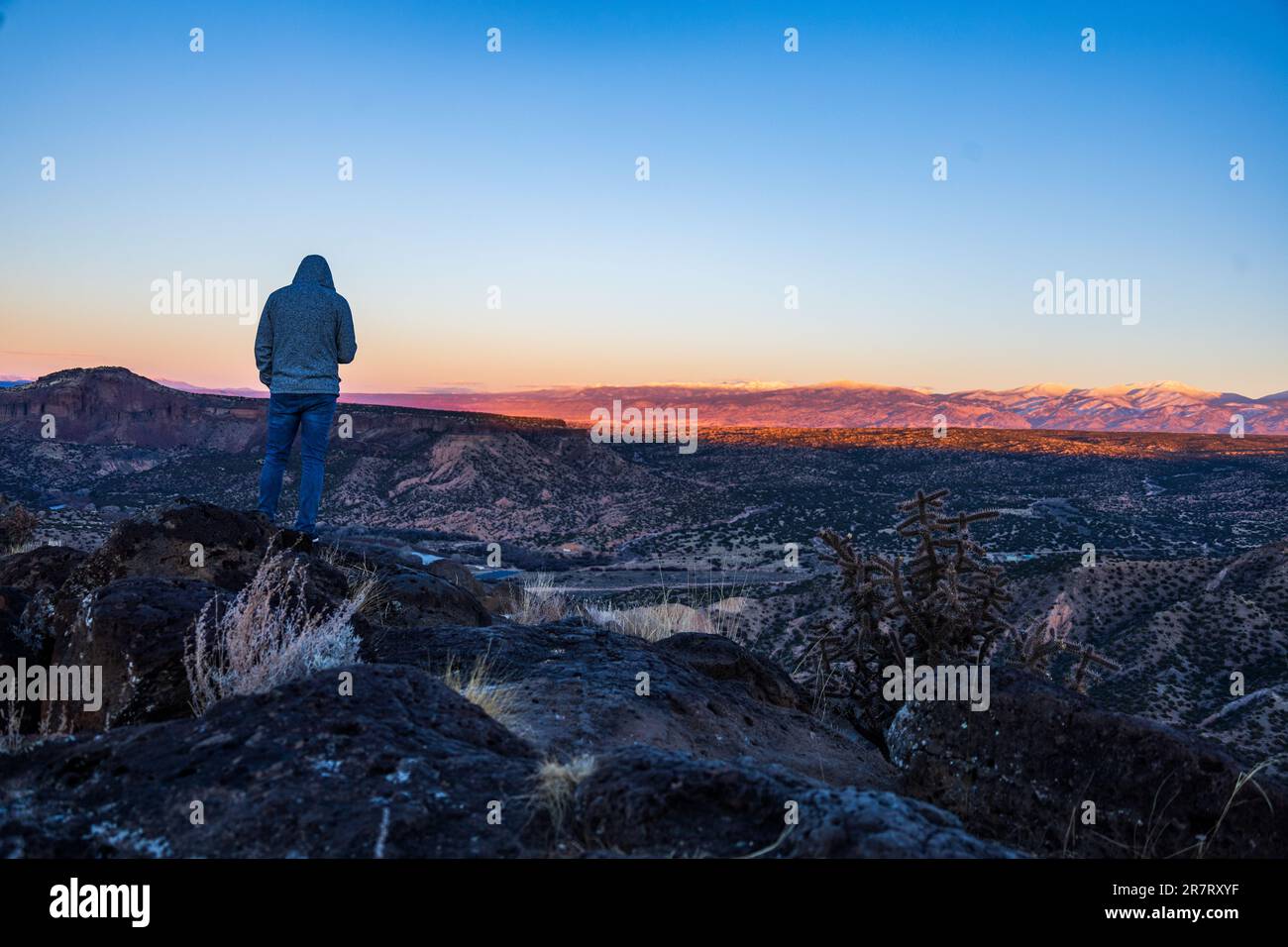 A silhouetted figure stands atop a hill as the sun sets over the ...