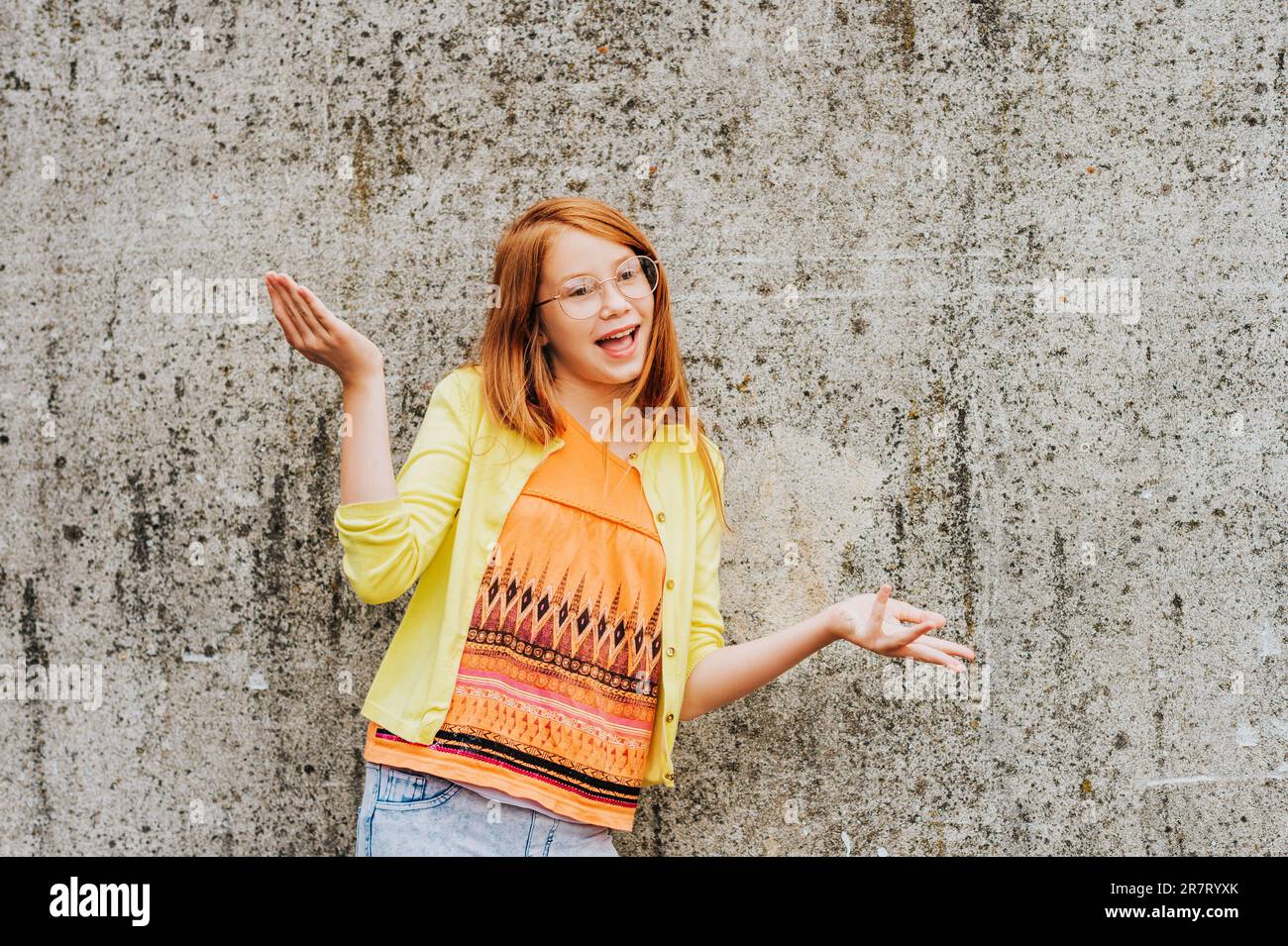 Outdoor portrait of pretty little girl with red hair, wearing orange t-shirt and yellow jacket Stock Photo