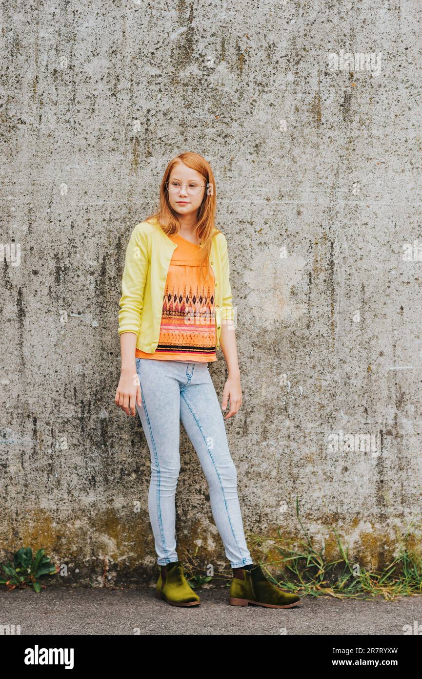 Outdoor portrait of pretty little girl with red hair, wearing orange t-shirt and yellow jacket Stock Photo